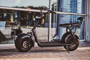 Trendy electrical scooter is parked near glass building at bright summer day.