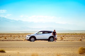 a man stands near a white jeep in the middle of a highway in the desert