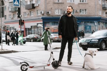 a man with a dog stands on the street near an electric scooter